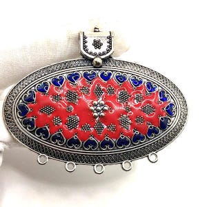 Puede incluir: Colgante ovalado de plata con centro de esmalte rojo, adornado con detalles azules en forma de corazón. El colgante presenta detalles intrincados y una argolla decorativa. El diseño incluye un motivo floral y bucles.