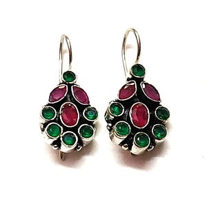May include: A pair of silver-toned earrings with a teardrop design. Each earring features a central oval ruby surrounded by smaller green and oval ruby gemstones. The earrings have a hook closure.