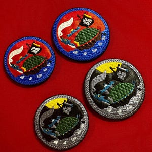 May include: Four embroidered patches with a pirate ship design. The patches feature a ship with a green turtle, a black flag, and blue water. The patches have red, blue, black, and silver borders.