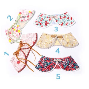 Puede incluir: Una selección de cinco collares decorativos para mascotas, cada uno con diseños florales y estampados únicos. Los collares presentan una gama de colores, incluyendo rojo, amarillo y azul, con detalles como botones y lazos.