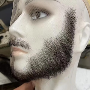 May include: A close-up of a mannequin head with a dark brown beard and mustache attached to a sheer lace base. The beard is full and well-defined, with a natural appearance.