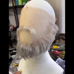 May include: A grey wig with a matching beard and moustache attached to a mesh base, designed to fit over the head. The wig is styled with short, textured hair and a full beard.