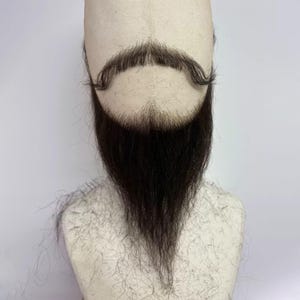 May include: A dark brown, full-length artificial beard and a matching handlebar-style moustache attached to a beige, fabric-covered mannequin head. The facial hair is styled with a pointed chin and a curved, groomed moustache shape.