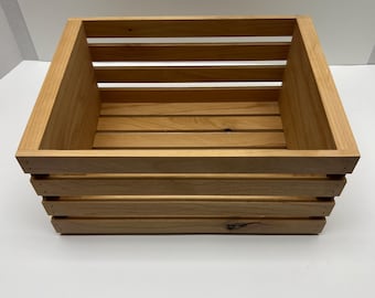 Peut inclure: Une caisse en bois brun clair de forme carrée. La caisse est construite avec des lattes horizontales sur les côtés et le fond, et du bois massif aux coins. Le bois a une finition naturelle.