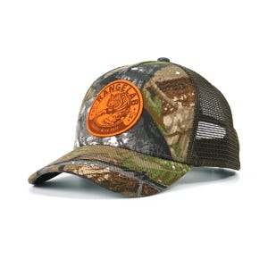 May include: A camouflage baseball cap with a brown mesh back and a curved brim. The front of the cap features a circular orange patch with a tiger graphic and the text "RANGELAB". The cap is designed for outdoor activities.
