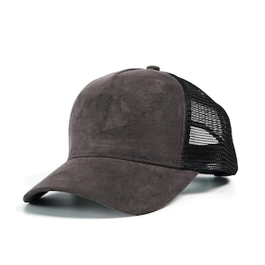 May include: A gray trucker hat with a suede-like front panel and a black mesh back. The hat has a curved brim and a button on top. The hat is designed to be worn by anyone.