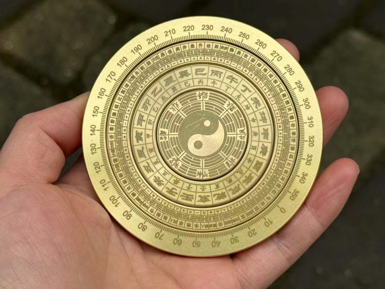 May include: A brass compass with intricate engravings and a Yin Yang symbol at the center. The compass features degree markings and Chinese characters around the perimeter. A traditional tool for navigation and divination.