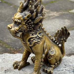 May include: A detailed brass sculpture of a mythical creature, possibly a dragon or a similar beast. The sculpture is in a seated position, with intricate details on its mane, scales, and claws. The brass has a golden hue.