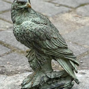 Peut inclure: Une sculpture détaillée, de couleur bronze, d'un faucon perché sur un rocher. L'oiseau présente des détails complexes sur les plumes et une expression sévère. La sculpture est patinée, avec des tons verts et bruns.