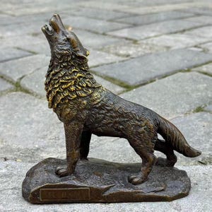 Könnte beinhalten: Bronzestatue eines heulenden Wolfes, montiert auf einem Steinsockel. Das Fell des Wolfes ist mit einem goldenen Farbton auf der Mähne detailliert. Die Statue ist ein dekorativer Artikel für die Inneneinrichtung.