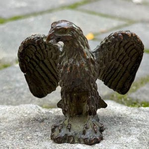 May include: Bronze eagle statue with outstretched wings. The sculpture has detailed feathering and stands on a textured base. The eagle's head is turned slightly to the side, giving it a dynamic pose. The statue is likely a decorative item.