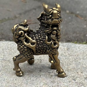 May include: A detailed bronze-colored figurine of a mythical creature, possibly a Qilin or similar, with a textured body and ornate detailing. The sculpture has horns and stands on four legs, showcasing a blend of artistry and cultural symbolism.