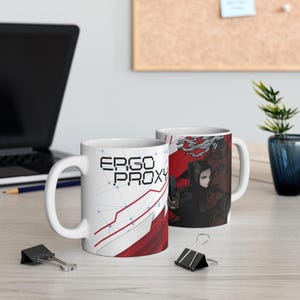 May include: Two white ceramic mugs. One displays the text "ERGO PROXY" in a geometric design with red and white accents. The second mug features a character illustration in red and black. A laptop and plant are in the background.