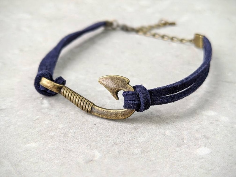 May include: A navy blue suede bracelet with a gold-toned fish hook charm.