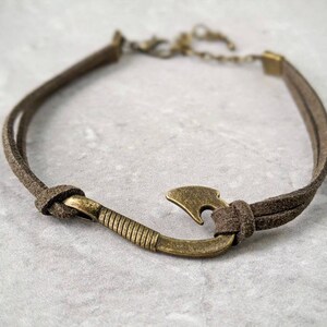 May include: A brown leather cord bracelet with a bronze fish hook charm.