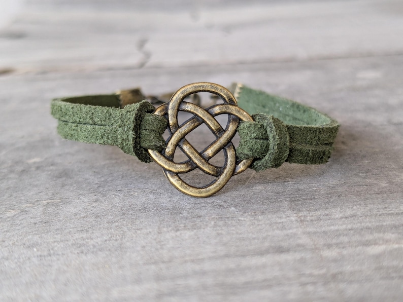 Pode incluir: Um bracelete de couro camur&ccedil;a verde com um fecho de n&oacute; celta dourado.