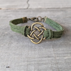 Pode incluir: Um bracelete de camur&ccedil;a verde com um amuleto de n&oacute; celta de lat&atilde;o.
