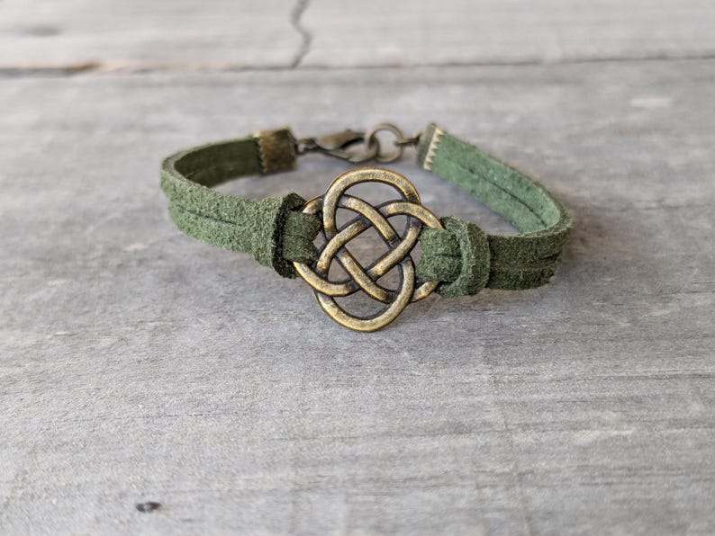 Pode incluir: Um bracelete de camur&ccedil;a verde com um amuleto de n&oacute; celta de lat&atilde;o.