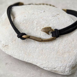 May include: A black suede cord bracelet with a bronze fish hook charm.