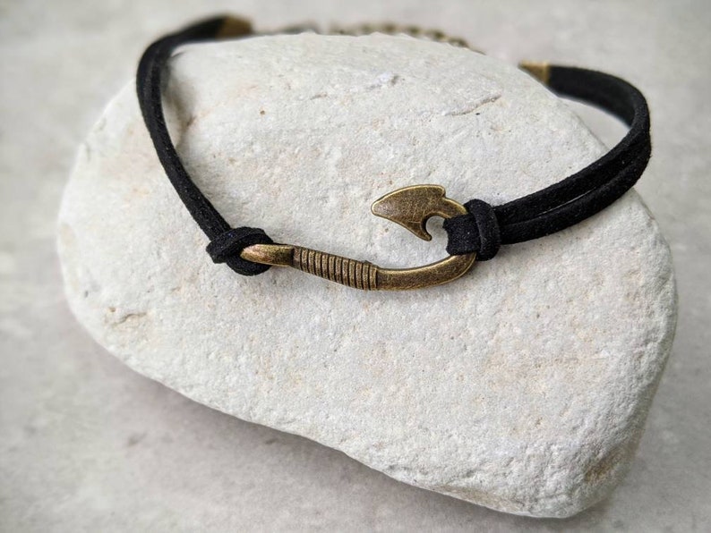 May include: A black suede cord bracelet with a bronze fish hook charm.