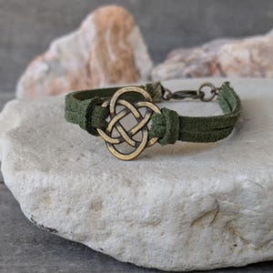 Pode incluir: Um bracelete de camur&ccedil;a verde com um fecho de n&oacute; celta dourado. O bracelete &eacute; ajust&aacute;vel e tem um fecho de encaixe.