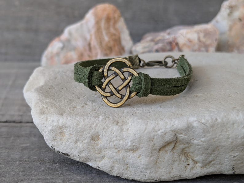 Pode incluir: Um bracelete de camur&ccedil;a verde com um fecho de n&oacute; celta dourado. O bracelete &eacute; ajust&aacute;vel e tem um fecho de encaixe.