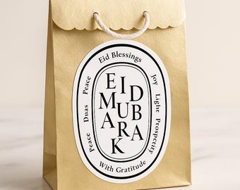 Könnte beinhalten: Eine goldene Geschenktüte mit einem wellenförmigen Rand und einem weißen Kordelgriff. Ein weißes ovales Etikett mit den Worten "Eid Mubarak" und "Eid Blessings" ist angebracht. Das Etikett enthält auch die Worte "Frieden, Freude, Licht, Wohlstand und Mit Dankbarkeit."