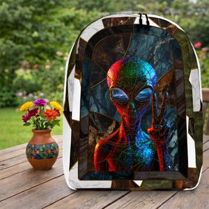 May include: A backpack featuring a vibrant, multi-colored alien graphic with a peace sign gesture, set against a dark, stained-glass style background with geometric patterns and white marble-like borders on the sides and top edges.