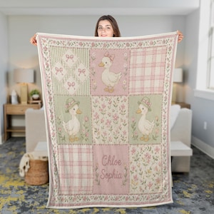 May include: A patchwork baby blanket in soft pink and green. The blanket features a repeating pattern of ducks wearing hats and bows, floral designs, and plaid squares. The name "Chloe Sophia" is printed on the blanket.