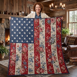 May include: A quilted blanket featuring the American flag design. The top left corner has a blue field with white stars. The stripes alternate between red and white floral patterns. The quilt is made of soft fabric.