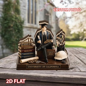 Op de afbeelding: Een afstudeerfiguur met een afgestudeerde in toga en hoed, zittend op een doos met het opschrift "Class of 2026". De basis luidt "University of California". Boeken, gereedschap en een helm zijn inbegrepen. De woorden "Custom Photo" en "2D Flat" zijn ook zichtbaar.