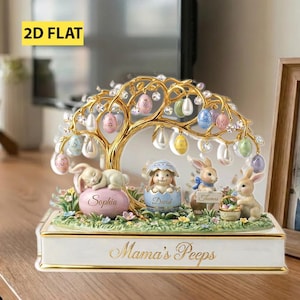 Puede incluir: Figura decorativa de Pascua con un árbol dorado adornado con huevos coloridos y detalles de cristal. La base tiene el texto "Mama's Peeps" e incluye figuras de conejitos y nombres. El diseño es ornamentado y festivo.