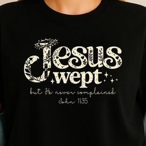 May include: Black t-shirt with the text "Jesus wept" in a decorative font, accompanied by the phrase "but He never complained" and the Bible verse John 11:35. The text is in a cream color.
