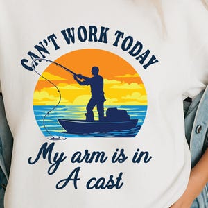 Könnte beinhalten: Weißes T-Shirt mit einem Angler auf einem Boot bei Sonnenuntergang. Der Text lautet "Can't work today, My arm is in a cast" in Marineblau. Das Design verwendet Orange, Gelb und Blau.