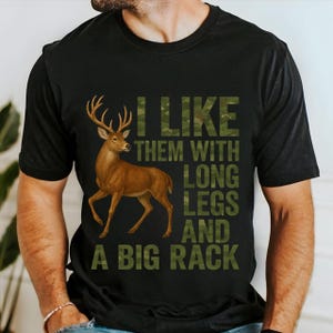 Könnte beinhalten: Schwarzes T-Shirt mit einer braunen Hirschillustration und Text in Camouflage-Schrift. Der Text lautet "I LIKE THEM WITH LONG LEGS AND A BIG RACK". Das T-Shirt hat einen Rundhalsausschnitt und ist ein Freizeitartikel.