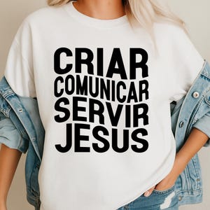 May include: White sweatshirt with the words "CRIAR COMUNICAR SERVIR JESUS" in bold black letters. The sweatshirt is a casual style, suitable for everyday wear. The text is vertically stacked.