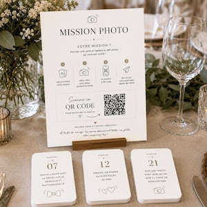 Peut inclure: Un panneau rectangulaire blanc intitulé MISSION PHOTO avec des instructions et un QR code, présenté sur un support en bois. Trois petites cartes blanches numérotées 07, 12 et 21 avec du texte français et des icônes sont posées devant.