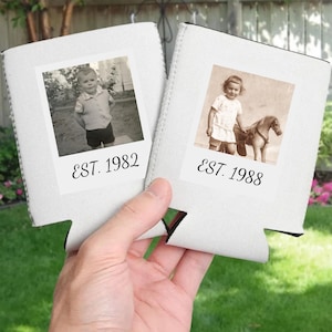 May include: Two white foam can coolers featuring square photo prints. The left cooler displays a black and white photo of a child with the text EST. 1982. The right cooler shows a sepia-toned photo of a child with a toy horse and the text EST. 1988.