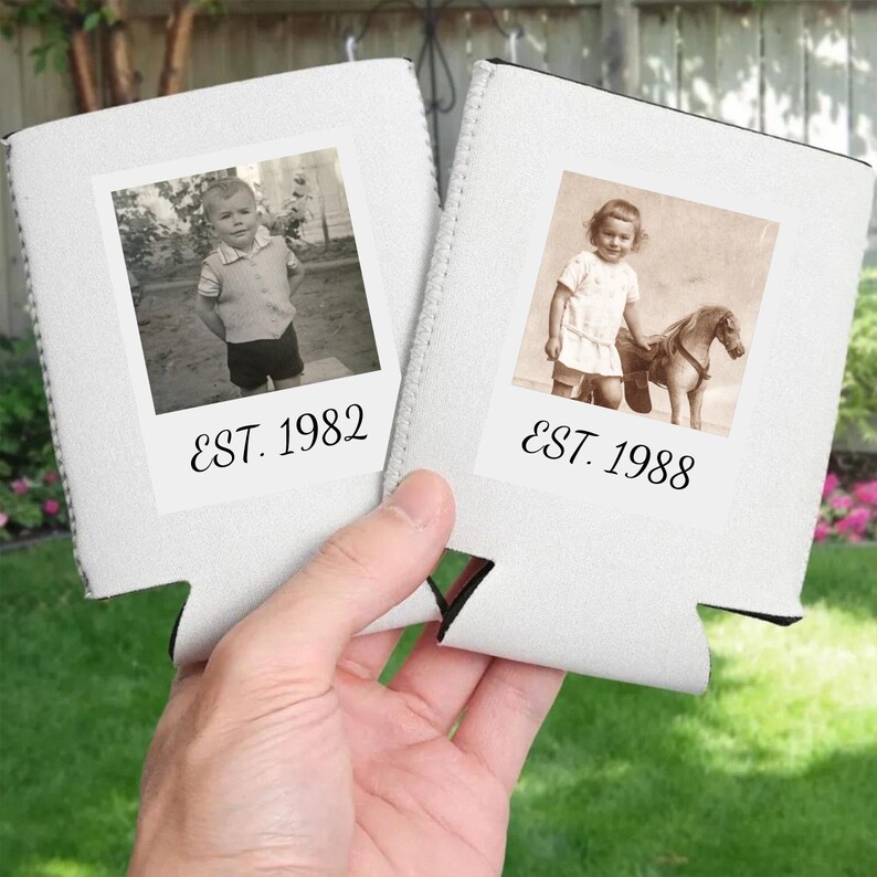 May include: Two white foam can coolers featuring square photo prints. The left cooler displays a black and white photo of a child with the text EST. 1982. The right cooler shows a sepia-toned photo of a child with a toy horse and the text EST. 1988.