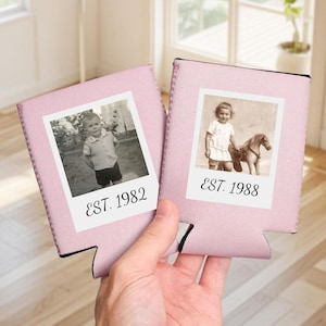 May include: Two light pink foam beverage insulators featuring a white square frame with a black and white photograph of a child. The left insulator displays a child and the text EST. 1982, while the right insulator shows a child with a toy horse and EST. 1988.
