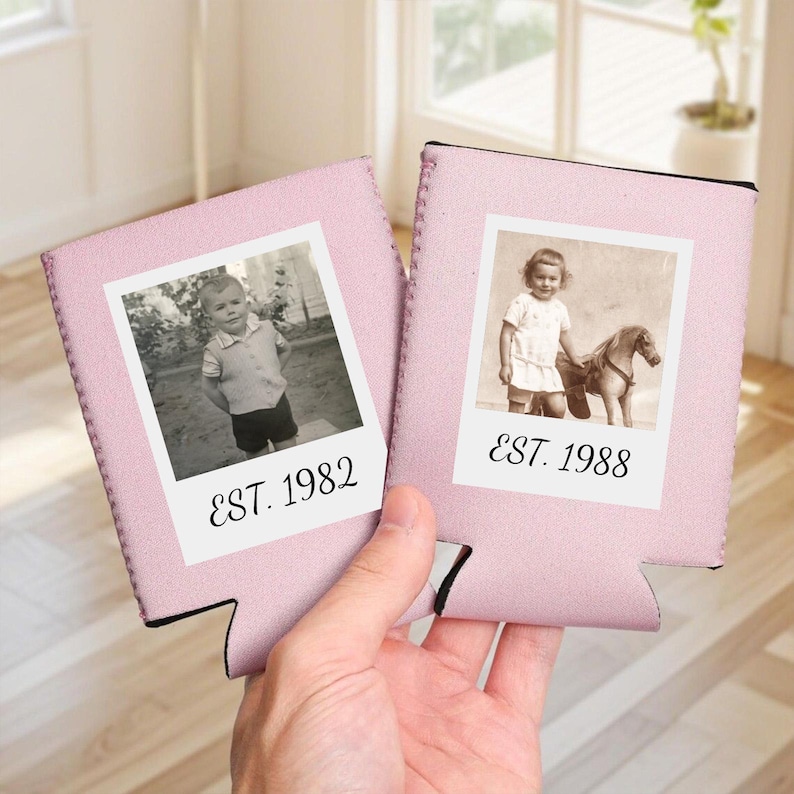 May include: Two light pink foam beverage insulators featuring a white square frame with a black and white photograph of a child. The left insulator displays a child and the text EST. 1982, while the right insulator shows a child with a toy horse and EST. 1988.