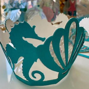 May include: A white ceramic mug with a black handle and the text "But First, Coffee" in a black, handwritten-style font. The mug is on a white surface.