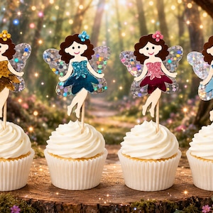 May include: Four cupcakes topped with fairy-shaped decorations. Each fairy has brown hair, a glittery dress in gold, teal, dark pink, or light blue, and iridescent wings. The figures are attached to wooden picks inserted into white frosting.