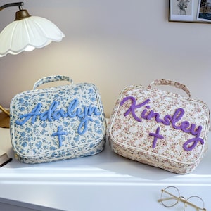 Puede incluir: Dos neceseres con estampado floral, uno azul y otro beige. La bolsa azul tiene el nombre "Adalyn" bordado en azul, y la bolsa beige tiene el nombre "Kinley" bordado en morado. Cada bolsa tiene un asa.