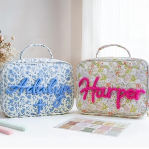 May include: Two personalized quilted bags with handles. One bag features a blue floral pattern with the name "Adalyn" in blue yarn. The other bag has a floral pattern with the name "Harper" in pink yarn. A color swatch card is also present.