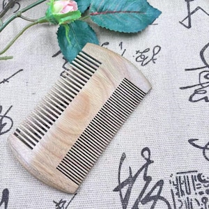 May include: A wooden comb with fine and wide teeth. The comb is made of light-colored wood and has a curved shape. The teeth are black and evenly spaced. The comb is designed for hair grooming.