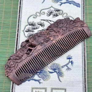 May include: A finely carved wooden comb with intricate floral and dragon designs. The comb is a rich brown color and features closely spaced teeth. The detailed carvings add a decorative element to the functional hair care tool.