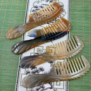 May include: Four handcrafted combs with wide teeth, made from a light brown material. The handles have a decorative, carved design. The combs are arranged on a patterned fabric and a green bamboo mat.