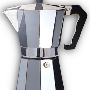 Op de afbeelding: Een geometrische koffiezetter in tinten grijs, zwart en wit. De handgreep is zwart en de bovenkant heeft een donkergrijze knop. Het ontwerp is modern en gestileerd, en lijkt op een mozaïek of collage.