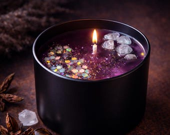 May include: A black cylindrical candle container holding purple wax with a lit white wick. The surface of the wax is decorated with iridescent hexagonal glitter on one side and several clear, irregular crystal-like stones on the other side.